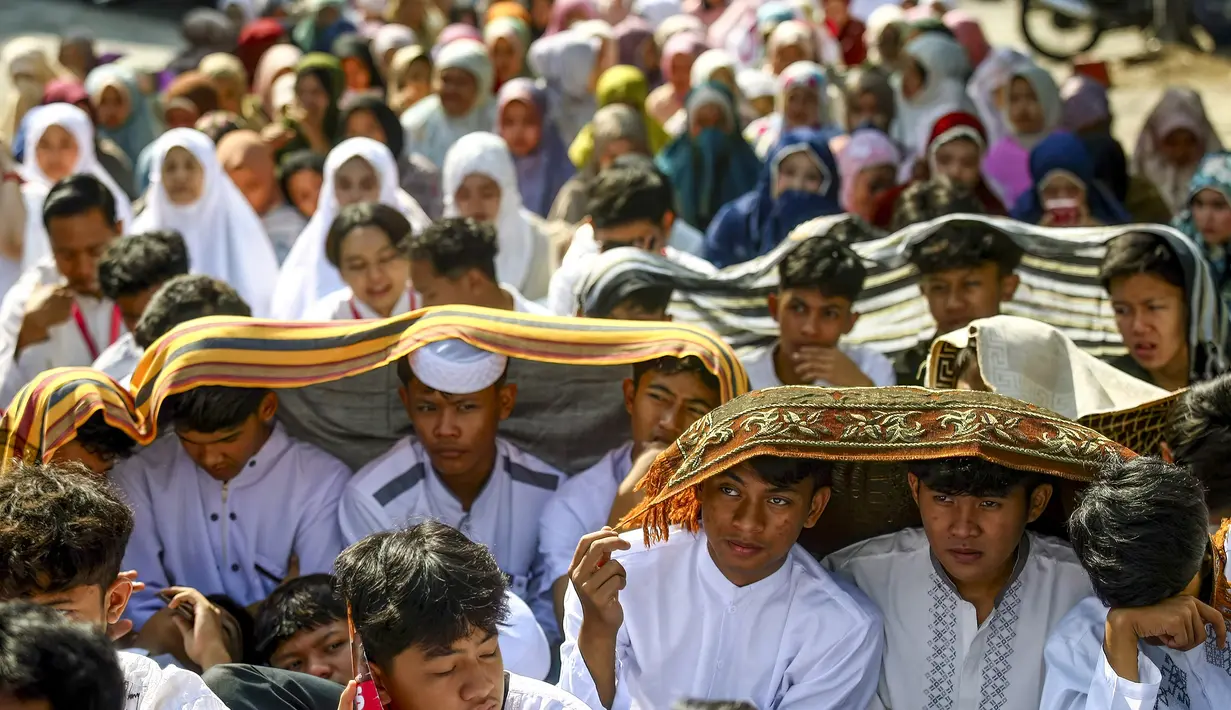 Sejumlah pelajar dan warga melindungi diri dari terik matahari saat mengikuti salat Istisqa untuk memohon turunnya hujan di tengah kekeringan berkepanjangan akibat fenomena El Niño di Malang, Jawa Timur, Kamis (22/10/2026). (Hayu Yudha/AFP)