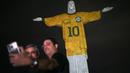 Sejumlah pengunjung berfoto bersama dengan Patung Kristus Sang Penebus (Christ the Redeemer) di Rio de Janeiro, Brasil saat diterangi gambar jersey dari legenda sepak bola Brasil, Pele sebagai penghormatan atas satu tahung kematian sang pemain pada Jumat, 29 Desember 2023. (AFP/Mauro Pimentel)