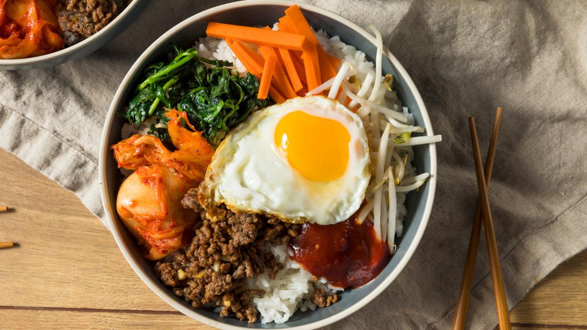Seporsi bibimbap campur sayur dengan aneka warna sayuran segar, telur mata sapi, dan saus gochujang khas Korea