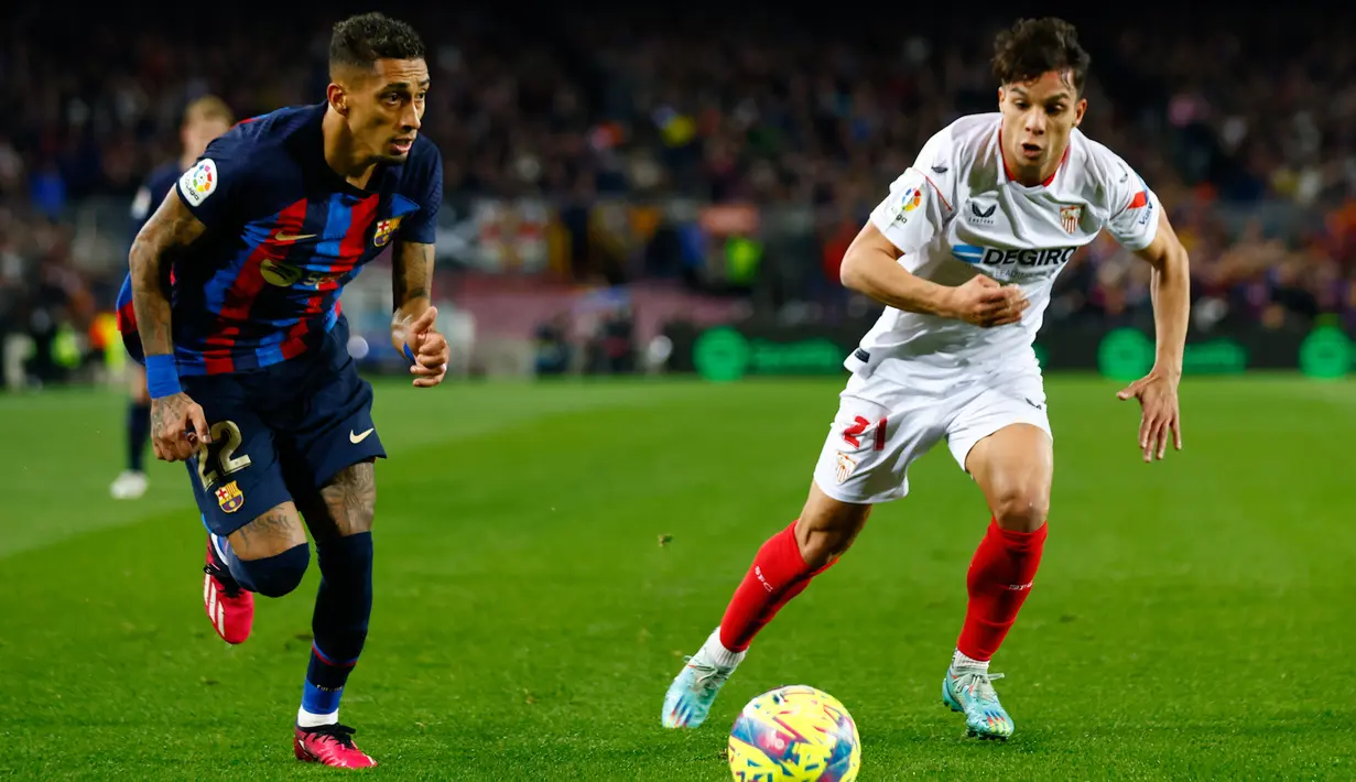 Pemain Barcelona, Raphinha (kiri) berusaha melewati hadangan pemain Sevilla, Oliver Torres dalam pertandingan pekan ke-20 La Liga 2022/2023 yang berlangsung di Camp Nou, Senin (6//2/2023). Raphinha berhasil mencetak satu gol bagi kemenangan 3-0 untuk Barcelona. (AP Photo/Joan Monfort)