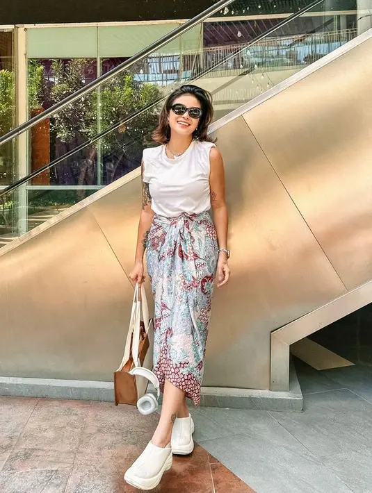 Ia juga tampil dengan atasan putih tanpa lengan dipadukan kain batik sebagai bawahan yang didominasi warna baby blue dan maroon. Serta sandal clog platform putihnya.  [@narinkovilda]