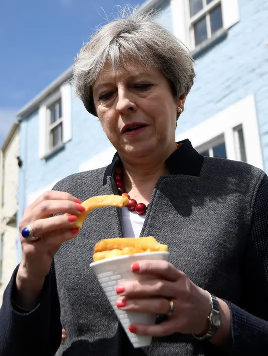 Perdana Menteri (PM) Inggris, Theresa May mencicipi beberapa keripik saat berhenti untuk kampanye di Mevagissey, Cornwall, Selasa (2/5). Theresa May melakukan kampanye dengan berkeliling jalanan di Cornwall. (AFP PHOTO/POOL/DYLAN MARTINEZ)