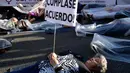 Seorang pengunjuk rasa berbaring di jalan dan memegang poster bertuliskan "Memenuhi kesepakatan!" saat melakukan aksi di Madrid, Spanyol (16/5). (AFP/Javier Soriano)