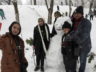 Orang-orang mengambil berswafoto dengan manusia salju ketika mereka menikmati salju di sebuah taman di Teheran utara, Iran (19/1/2020). Salju tebal menutupi jalan-jalan Teheran, menyebabkan penundaan penerbangan dan munutup sekolah, kata pihak berwenang di ibukota Iran. (AP Photo / Vahid Salemi)