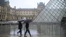 Orang-orang berjalan melintasi museum Louvre di Paris pada Minggu (1/3/2020). Louvre, museum yang paling banyak dikunjungi di dunia, ditutup sementara untuk pengunjung setelah para staf menolak bekerja di tengah kekhawatiran terjangkit virus corona tipe baru, Covid-19. (AP/Rafael Yaghobzadeh)