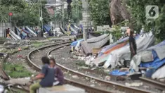 Sejumlah tunawisma beraktivitas di dekat gubuknya yang berada di bantaran rel kereta api kawasan Senen, Jakarta, Minggu (14/2/2021). Setelah sempat ditertibkan, puluhan bangunan semipermanen yang beratapkan terpal dan beralas kardus milik tunawisma kembali menjamur. (merdeka.com/Iqbal S. Nugroho)
