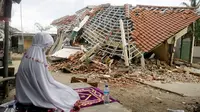 Seorang wanita berdoa di depan puing-puing bangunan di Lombok Barat, Nusa Tenggara Barat (NTB), Sabtu (11/8). BNPB menyatakan gempa Lombok hingga saat ini telah menewaskan 387 orang. (AP Photo/ Firdia Lisnawati)