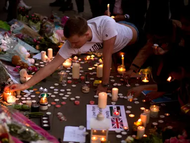 Seorang pria menyalakan lilin sehari setelah serangan bunuh diri di sebuah konser Ariana Grande di Albert Square, Manchester, Inggris, (23/5). Kejadian ini menyebabkan 22 orang tewas  dan melukai 119 lainnya. (AP Photo/Emilio Morenatti)