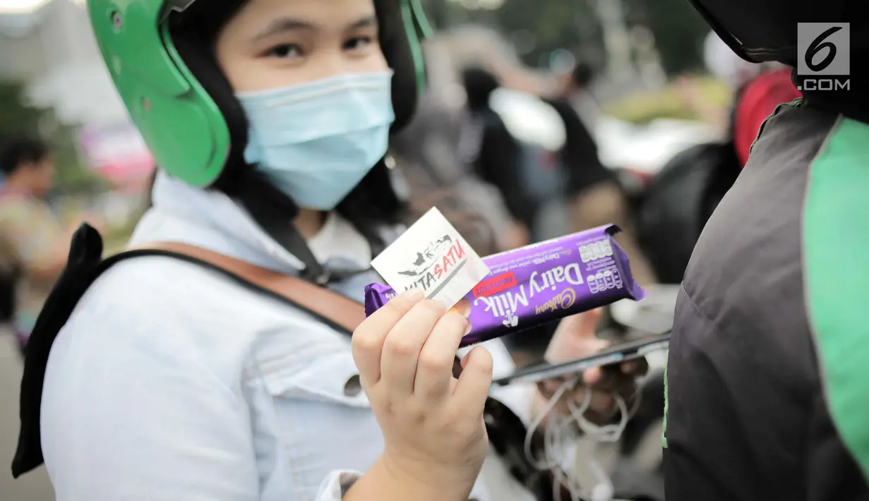 Penumpang ojek online menerima cokelat dari Kita Satu Relawan Milenial Jokowi-Amin di kawasan Patung Kuda, Jakarta, Kamis (18/4). Kegiatan tersebut sebagai bentuk terima kasih kepada seluruh anak bangsa yang telah ikut memberikan suaranya di TPS. (Liputan6.com/Faizal Fanani)
