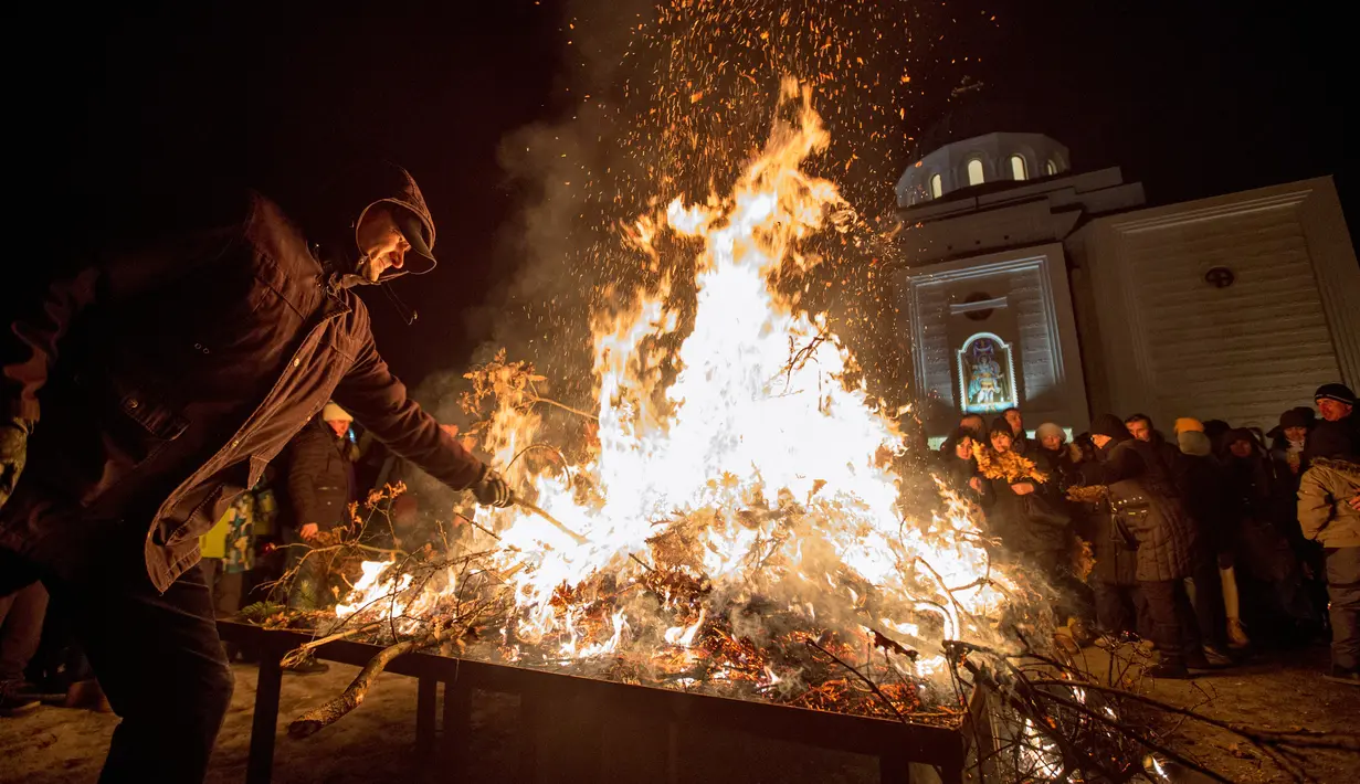 Seorang pria membakar ranting pohon oak kering  atau Yule log selama perayaan Hari Natal Ortodoks di Belgrade, Serbia (6/1). Umat Kristen Ortodoks di Serbia memiliki tradisi yang cukup unik dalam merayakan Natal, yaitu membakar ranting. (AFP/Oliver Bunic)