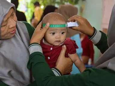 Seorang tenaga kesehatan mengukur lingkar kepala bayi selama program imunisasi massal di Surabaya pada 15 September 2025. (Juni KRISWANTO/AFP)