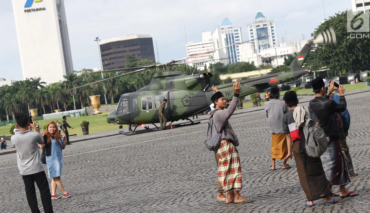 Warga berpose berlatar helikopter TNI di kawasan Monumen Nasional, Jakarta, Jumat (19/4). Libur panjang perayaan Paskah 2019 dimanfaatkan warga untuk berwisata di kawasan Monumen Nasional. (Liputan6.com/Helmi Fithriansyah)