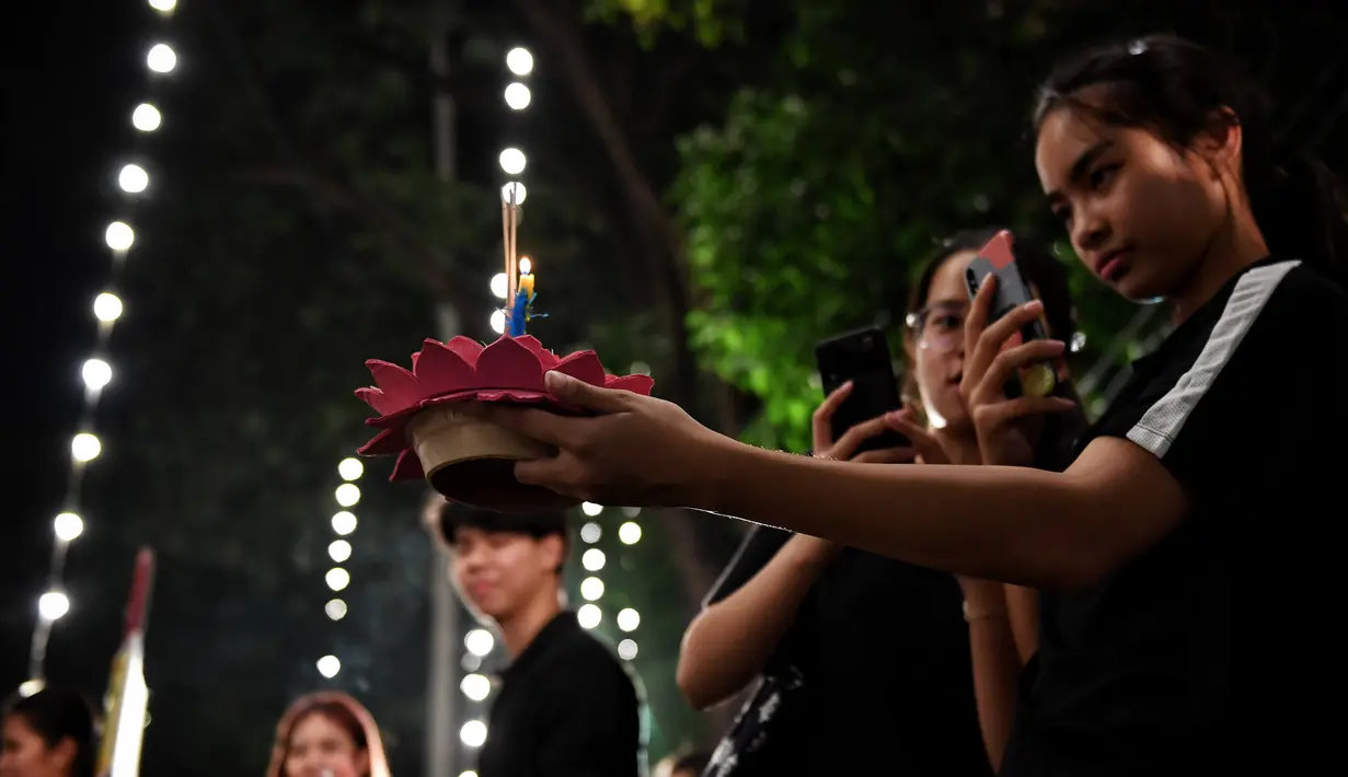 Seorang perempuan mengambil gambar 'krathong' sebelum dihanyutkan untuk menandai festival Loy Krathong di sebuah danau di Bangkok, Thailand,  Senin (11/11/2019). Selain melarung ke air, Loy Krathong juga diisi dengan pelepasan lentera ke udara. (Lillian SUWANRUMPHA / AFP)