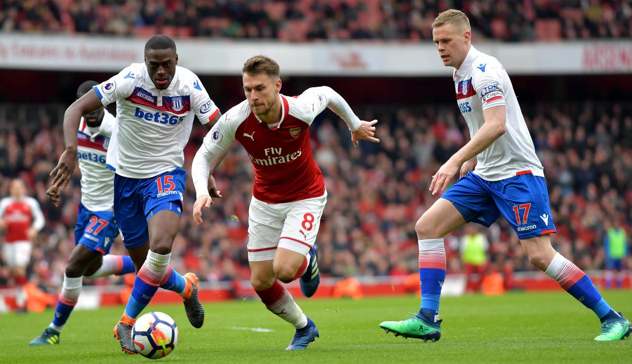 Gelandang Arsenal, Aaron Ramsey, melewati kepungan pemain Stoke pada laga Premier league di Stadion Emirates, London, Minggu (1/4/2018). Arsenal menang 3-0 atas Stoke. (AFP/Oliver Greenwood)