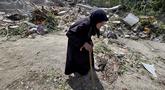 Seorang wanita lanjut usia berjalan melewati petugas pertahanan sipil Lebanon yang sedang mencari korban di antara reruntuhan, sehari setelah serangan Israel di desa Deir Qanun al-Nahr, Lebanon Selatan, pada Rabu 20 Mei 2026. (KAWNAT HAJU/AFP)