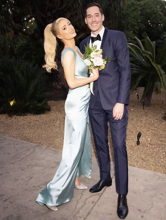 Menjadi Bridesmaid, Paris mengenakan gaun satin slit lengan  sleeveless, dipadukan stiletto heels silvernya. Sang suami pun kembali mengenakan setelan suit.(@parishilton)