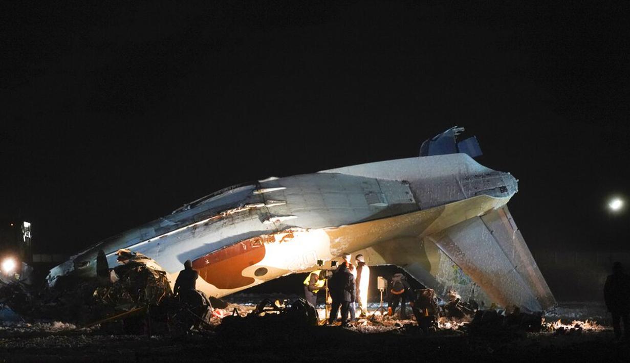 Pekerja darurat bekerja di samping pesawat Antonov An-26 yang jatuh di Bandara Almaty, Kazakhstan, Sabtu (13/3/2021). Saat terjatuh, gumpalan asap mengepul dari lokasi kecelakaan. (AP Photo/Vladimir Tretyakov)