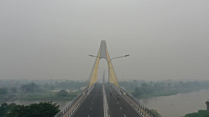 Gambar udara menunjukkan sebuah jembatan ketika kabut asap pekat menyelimuti Pekanbaru, Riau, Minggu (15/9/2019). Kabut asap yang menyelimuti Kota Pekanbaru makin pekat akibat kebakaran hutan dan lahan di Riau, Jambi, serta Sumatera Selatan. (ADEK BERRY/AFP)