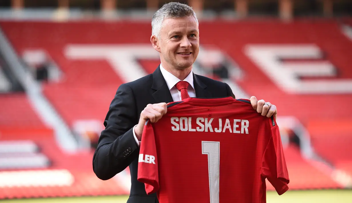 Ole Gunnar Solskjaer menunjukkan jersey Manchester United saat konferensi pers di Stadion Old Trafford, Inggris, (28/3). MU mengontrak Solskjaer selama tiga tahun. (AFP Photo/Oli Scarff)
