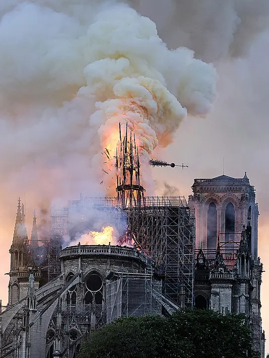 Api dan asap mengepul dari puncak menara Gereja Katedral Notre-Dame dalam kebakaran di pusat kota Paris, Prancis, pada Senin (15/4). Hingga kini belum diketahui pasti apa yang menjadi penyebab utama terbakarnya salah satu situs warisan dunia UNESCO tersebut. (AP Photo/Diana Ayanna)