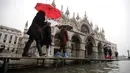 Sejumlah warga berjalan melewati papan saat gelombang pasang membuat banjir depan Basilika Santo Markus, Venesia, Italia, Selasa (12/11/2019). Venesia dilanda banjir akibat gelombang pasang setinggi 127 cm. (AP Photo/Luca Bruno)