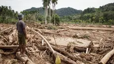 Seorang pria melihat kerusakan yang disebabkan oleh banjir yang membawa sisa-sisa pembalakan liar di Pelangai Gadang, Sumatera Barat, pada Sabtu 15 Maret 2025. (REZAN SOLEH/AFP)