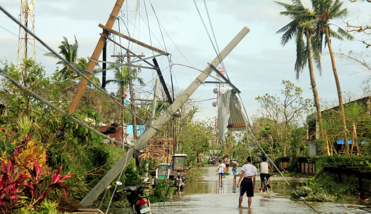 Sejumlah warga berjalan dibawah tiang listrik yang roboh akibat angin kencang yang disebabkan Topan Nock-ten di Kota Iriga Camarines Sur, Filipina tengah (27/12). (REUTERS/Romeo Ranoco)