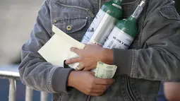 Jonatan Camacho membawa dua tangki oksigen setelah diisi ulang untuk keluarganya yang sakit COVID-19 di Mexico City pada 27 Desember 2020. Lonjakan pasien terinfeksi virus corona yang dirawat membuat toko pasokan medis kekurangan pasokan isi ulang tabung oksigen. (AP Photo/Ginnette Riquelme)