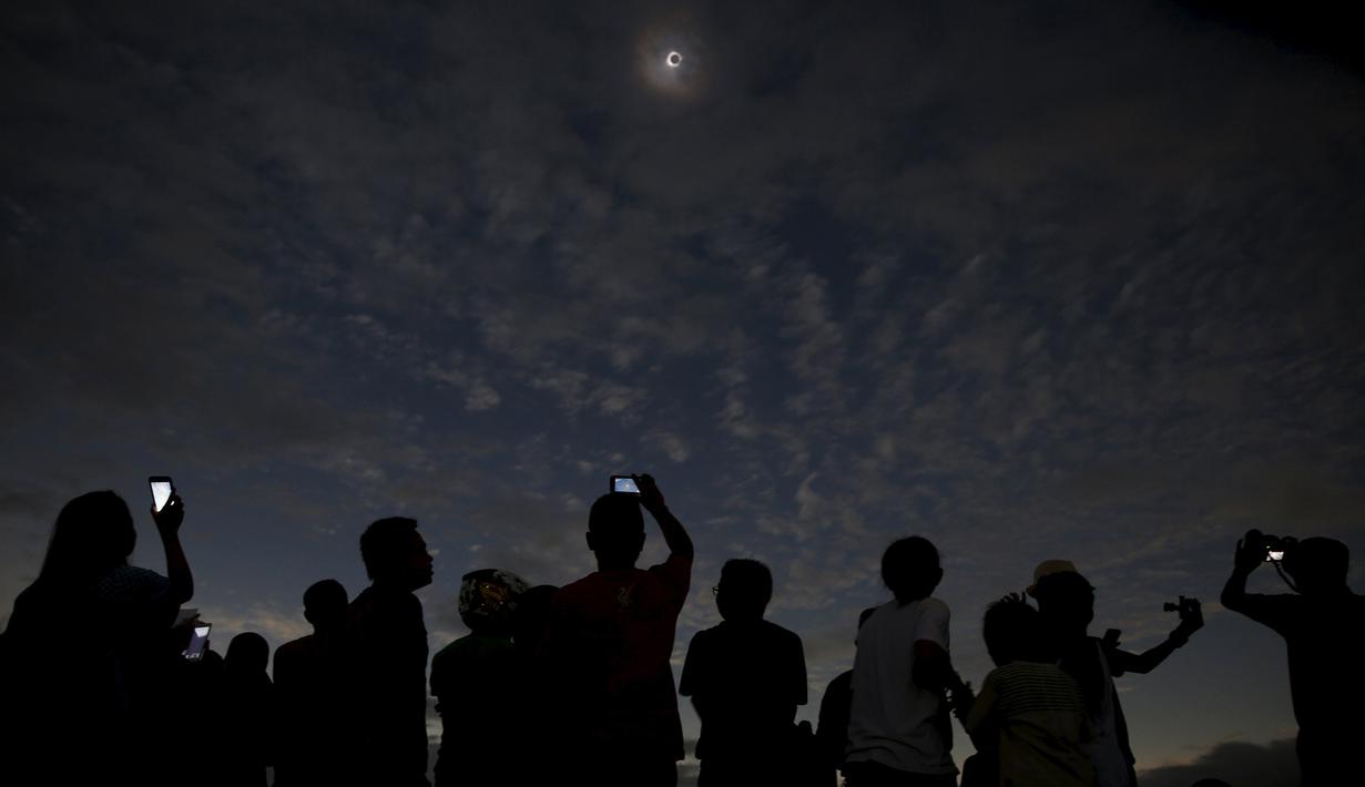Sejumlah orang melihat dan mengambil gambar dari fenomena Gerhana Matahari Total (GMT) di pantai di pulau Ternate, Indonesia, Rabu (9/3/2015). (REUTERS / Beawiharta)