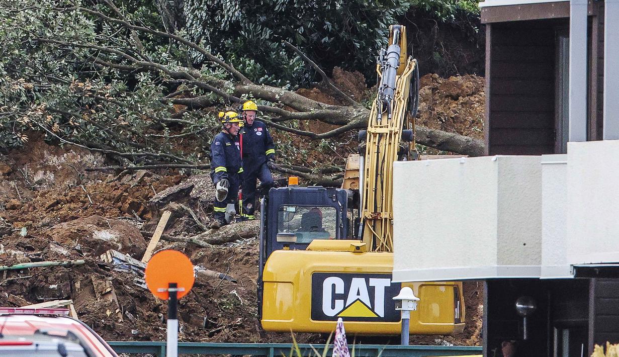 Polisi dan petugas yang berdiri setelah tanah longsor sementara pencarian sedang dilakukan oleh layanan darurat setempat untuk orang hilang di Gunung Maunganui, Tauranga, Selandia Baru pada Kamis 22 Januari 2026. Hujan lebat yang mengguyur Selandia Baru menyebabkan sejumlah kerusakan dan memicu longsor. (DJ MILLS/AFP)