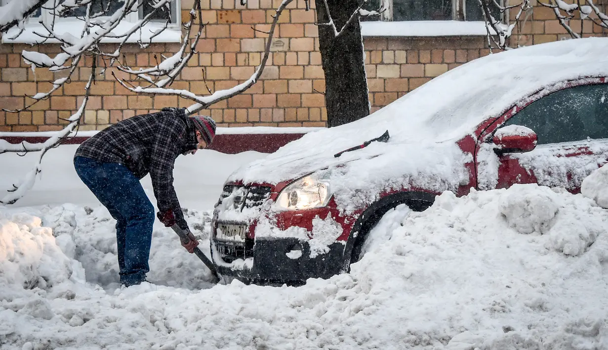 Seorang pria menggali untuk memindahkan mobilnya usai dilanda badai salju di Moskow (5/2). Suhu udara di sana mencapai minus 34 derajat celcius. (AFP/Vasily Maximov)