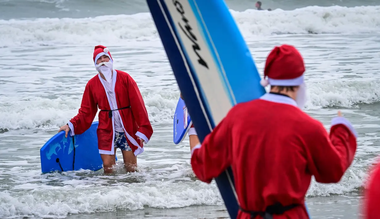 Seorang pengunjung berkostum Sinterklas berselancar dalam acara Surfing Santa yang berlangsung di Pantai Cocoa, Florida, Amerika Serikat, Selasa (24/12/2024) waktu setempat. (AFP/Giorgio Viera)