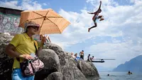 Turis menggunakan payung berada di Danau Jenewa di Saint Saphorin, Swiss barat saat gelombang panas melanda seluruh Eropa utara (31/7). Wilayah yang terkena dampak gelombang panas Valais, Danau Jenewa, Ticino dan Basel. (AFP Photo/Fabrice Coffrini)