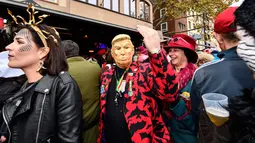 Seorang pria dengan topeng Donald Trump bersuka cita saat puluhan ribu orang menyambut dimulainya musim karnaval di jalan-jalan Kota Cologne, Jerman, Senin (11/11/2019). Tradisi ini akan dimulai tepat pada jam 11.11, tanggal 11, dan bulan sebelas. (AP Photo/Martin Meissner)