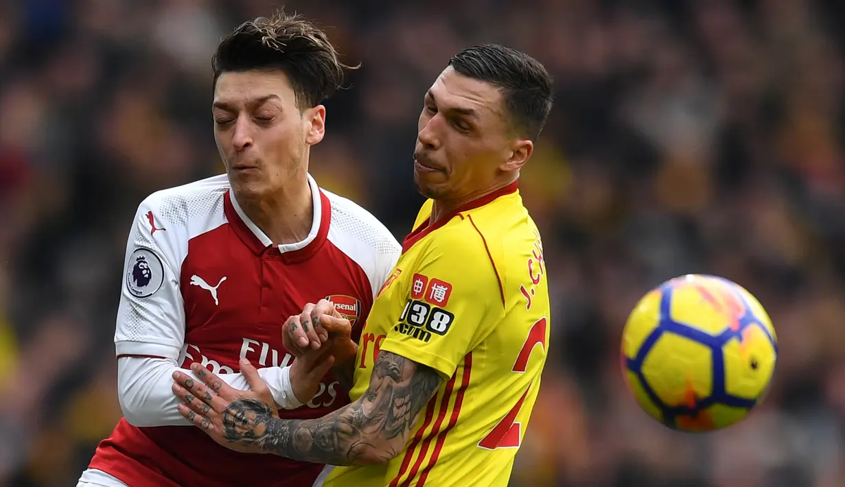 Gelandang Arsenal Mesut Ozil berebut bola dengan pemain Watford, José Holebas pada lanjutan pertandingan Liga Inggris di Emirates Stadium, Minggu (11/3). Kemenangan telak sukses dibukukan Arsenal usai mengalahkan Watford 3-0. (Ben STANSALL / AFP)
