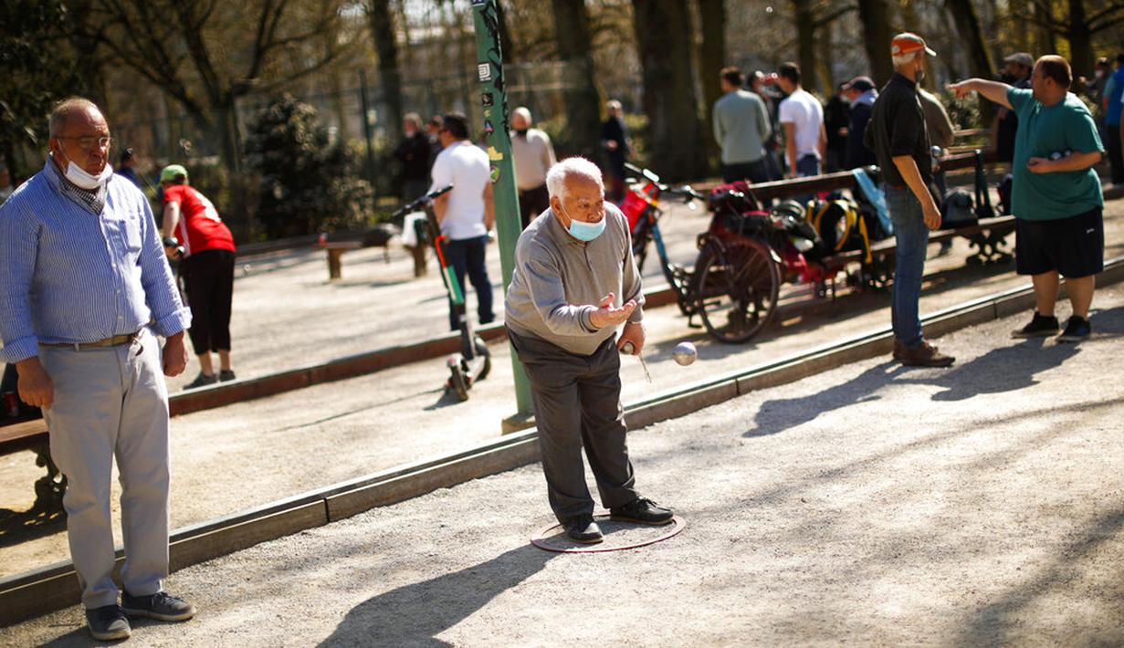 Seorang pria mengenakan masker untuk mencegah penyebaran COVID-19 saat memainkan boule di Taman Cinquantenaire, Brussel, Belgia, Senin (29/3/2021). Belgia kembali memberlakukan lockdown ketat sebagai tanggapan atas lonjakan infeksi COVID-19 yang mengkhawatirkan. (AP Photo/Francisco Seco)