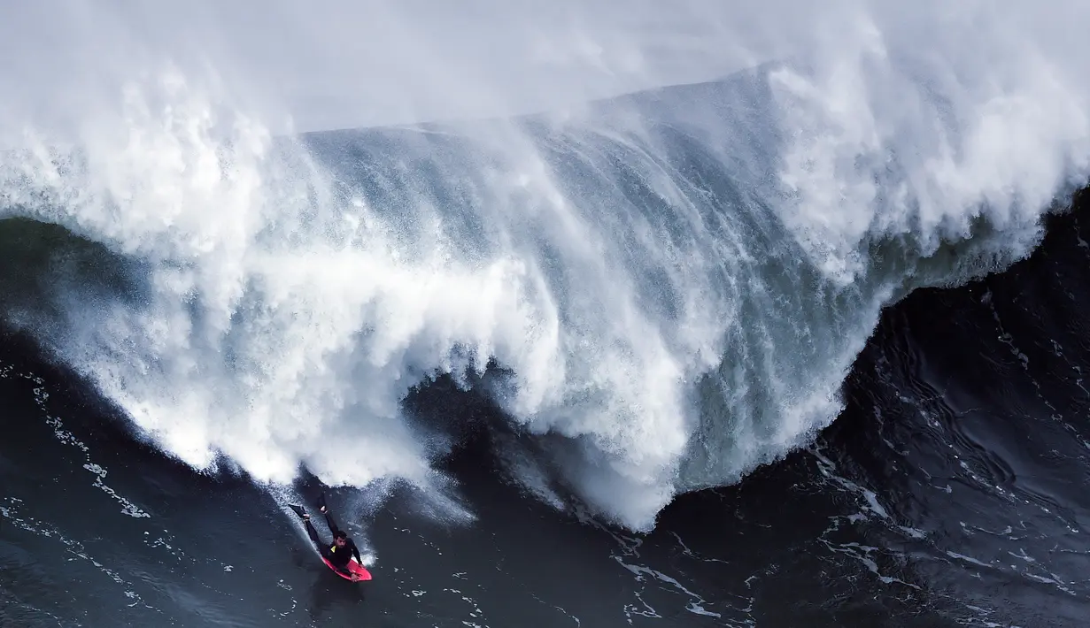 Seorang peselancar bersiap menyambut kejaran ombak besar dibelakangnya saat berselancar di Praia do Norte di Nazare, Portugal (19/11). Selancar merupakan sebuah olahraga yang dilakukan di atas ombak yang tinggi. (AFP/Patricia De Melo Moreira)