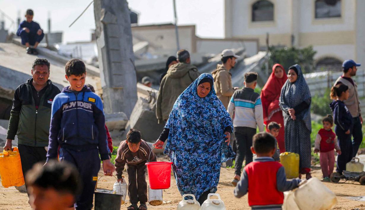 Sekitar 67% fasilitas air dan sanitasi di kota Gaza dilaporkan hancur atau rusak akibat konflik berkepanjangan antara Israel dan Hamas. Tampak dalam foto, warga mengisi wadah air dari tangki air portabel di kamp pengungsi Palestina Maghazi, Jalur Gaza tengah pada Rabu 11 Februari 2026. (Eyad BABA/AFP)