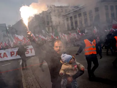 Seorang pria menggendong seorang anak dan melambaikan obor saat ribuan orang berkumpul di pusat kota untuk pawai Hari Kemerdekaan tahunan di Warsawa, Polandia, 11 November 2022. Pawai ini diselenggarakan oleh kelompok-kelompok nasionalis yang telah ditandai dengan kekerasan dalam beberapa tahun terakhir. (AP Photo/Michal Dyjuk)