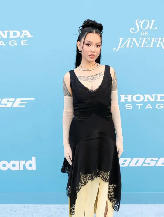 Bella Poarch tampil dalam balutan sleeveless dress warna hitam dengan detail boatneck warna hitam. Dress-nya dipadukan dengan sarung tangan warna putih. [@muchofficial].