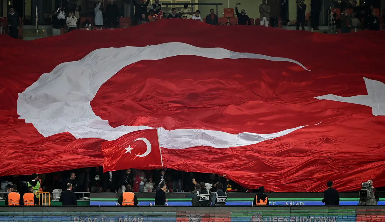 Pendukung Turki membentangkan bendera raksasa saat laga Grup D Kualifikasi Euro 2024 melawan Latvia di Konya Buyuksehir Belediye Stadium, Konya, Turki, Senin (16/10/2023) dini hari WIB. (AFP/Ozan Kose)