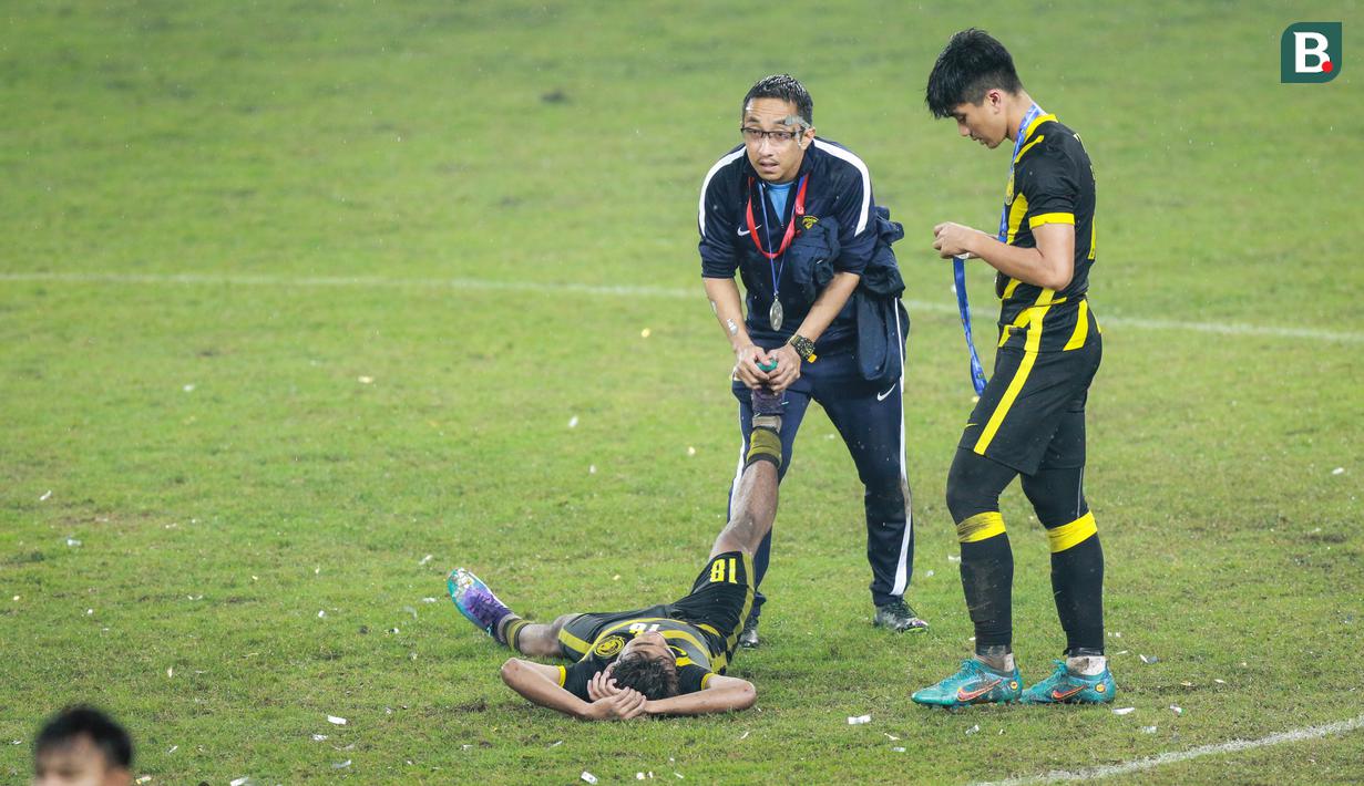 Pemain Timnas Malaysia U-19, Adam Farhan Mohd Faizal (kiri) tengah mendapatkan perawatan dari salah satu official tim saat timnya merayakan juara Piala AFF U-19 2022 di Stadion Patriot Candrabhaga, Bekasi, Jumat (15/07/2022). (Bola.com/Bagaskara Lazuardi)