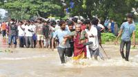 Orang-orang menyeberang melalui jalan yang banjir di Nellore, di negara bagian Andhra Pradesh, India selatan, Sabtu, 20 November 2021. Lebih dari selusin orang tewas dan puluhan lainnya dilaporkan hilang di Andhra Pradesh setelah berhari-hari hujan lebat, kata pihak berwenang. (AP Photo)