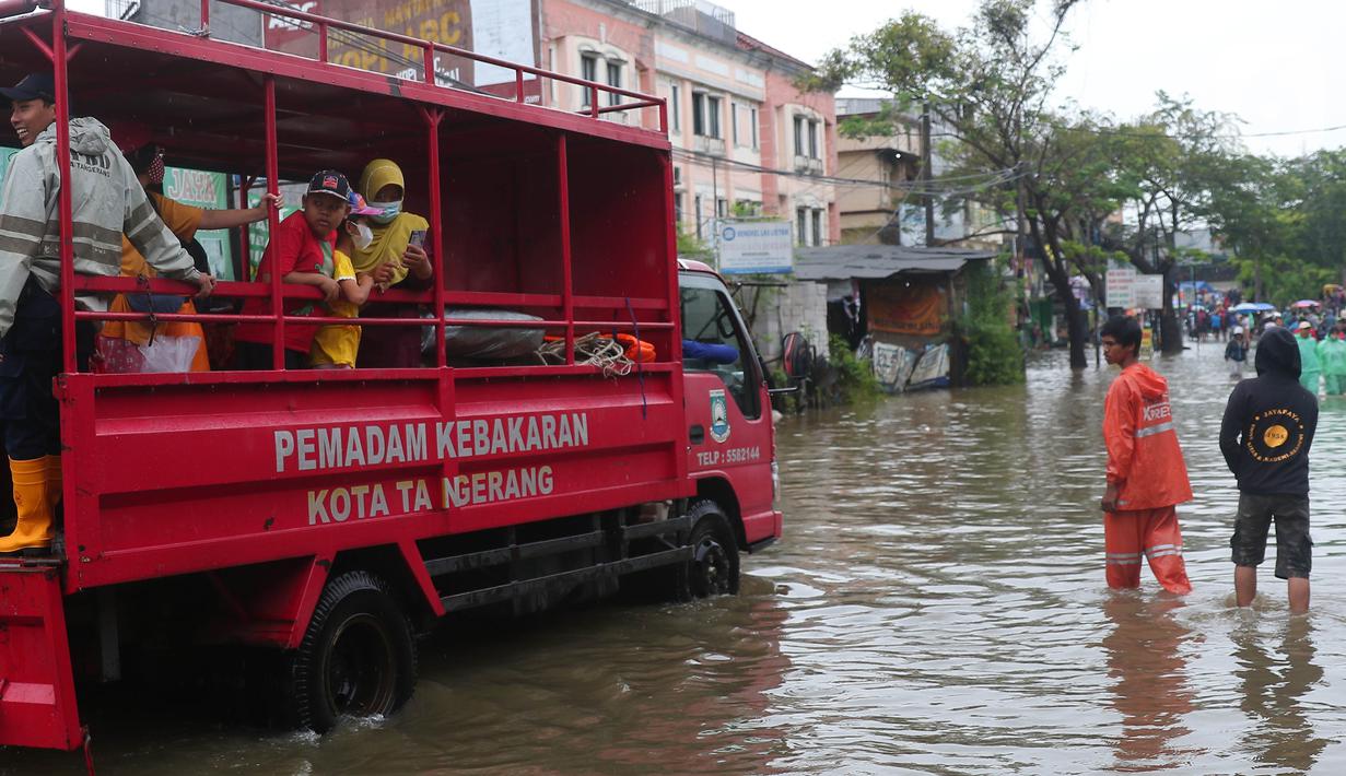 Warga menaiki mobil milik pemadam kebakaran Kota Tangerang untuk melintasi genangan air ketika banjir merendam Jalan KH. Hasyim Ashari, Tangerang, Banten, Sabtu (16/7/2022). Akibat luapan kali angke ruas jalan yang menghubungkan Tangerang-Jakarta itu terputus akibat banjir. (Liputan6.com/Angga Yuniar)