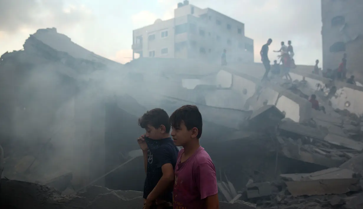 Dua remaja berada di puing-puing bangunan yang hancur akibat serangan udara Israel di Kota Gaza, Palestina, (9/8). Israel dan Hamas telah berperang tiga kali sejak Hamas menguasai Gaza pada 2007. (AP Photo/Khalil Hamra)