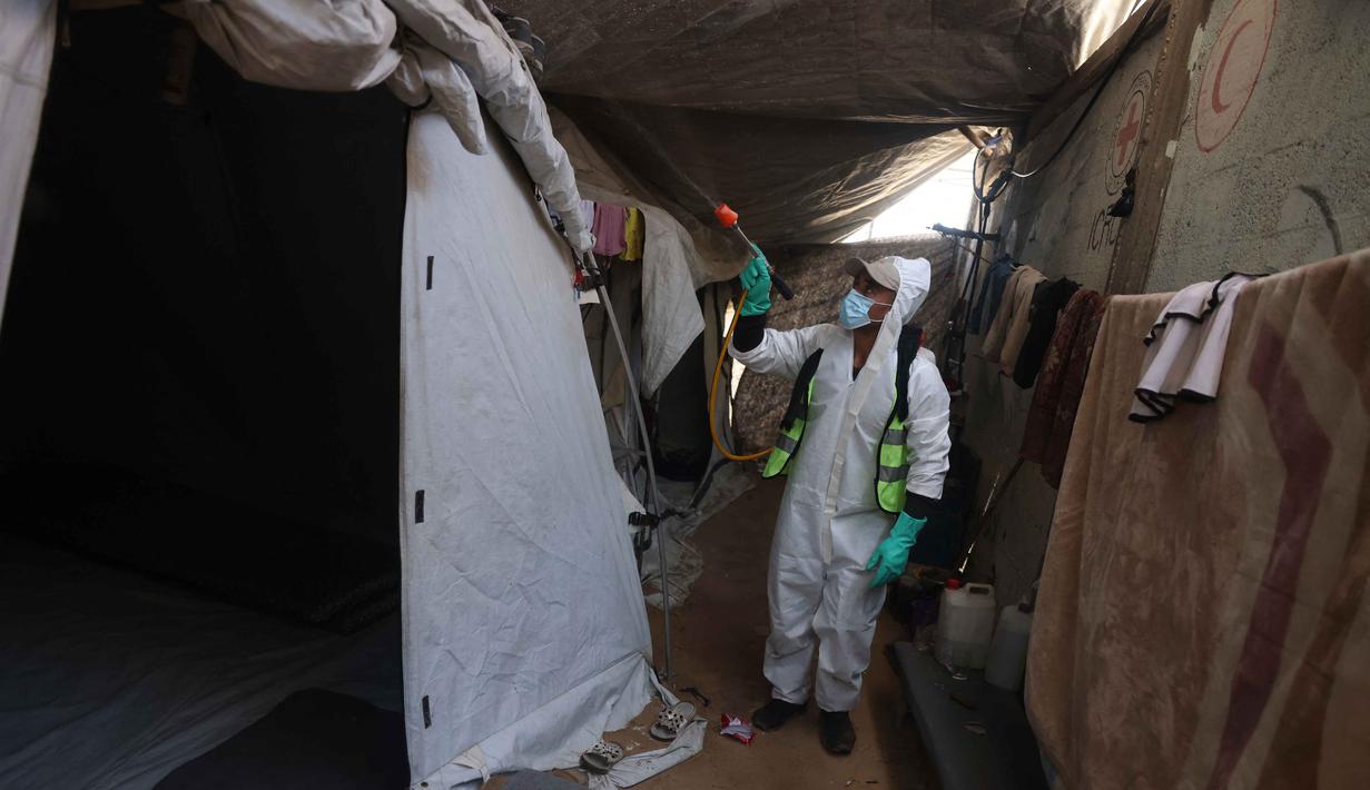 Seorang pengungsi Palestina menyemprotkan cairan disinfektan pada jalan setapak dan tenda-tenda untuk membasmi serangga dan hewan pengerat di kamp pengungsian Khan Yunis, Jalur Gaza Selatan pada Rabu 22 April 2026. Krisis kemanusiaan di Gaza kian memburuk. (Bashar Taleb/AFP)