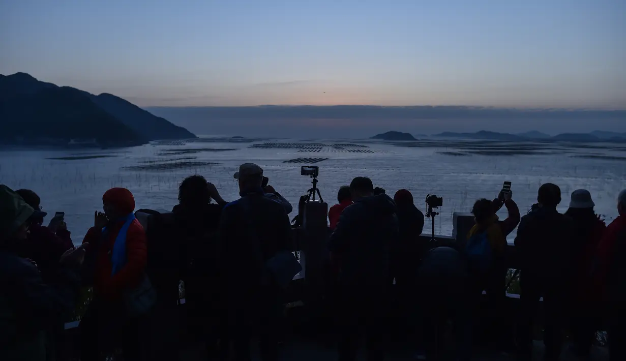 Wisatawan menyaksikan matahari terbit di Niu Yu, Xiapu, Provinsi Fujian, China, Jumat (13/12/2019). Xiapu menjadi daya tarik tersendiri bagi fotografer pemula karena jauh dari gedung pencakar langit dan hiruk pikuk kota-kota besar di China. (RETAMAL HECTOR/AFP)