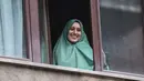 Petugas bantuan Italia bernama Silvia Romano, yang dibebaskan oleh militan Somalia, tersenyum dari jendela setelah tiba di rumahnya di Milan, 11 Mei 2020. Silvia, 25 tahun, memutuskan masuk Islam setelah dirinya diculik dari kota pesisir tenggara Kenya pada November 2018. (AP/Luca Bruno)