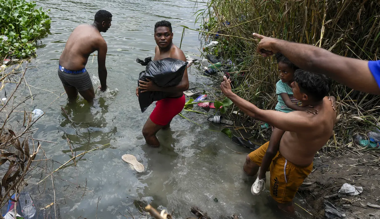 Dengan tenggat waktu larut malam yang semakin dekat, para migran di Meksiko melepaskan pakaian mereka sebelum menuruni jurang curam menuju Rio Grande, memegangi kantong plastik berisi pakaian. (AP Photo/Fernando Llano)