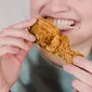 Seorang wanita sedang menggigit ayam kentucky. (Liputan6.com/Pexels/Tim Samuel)